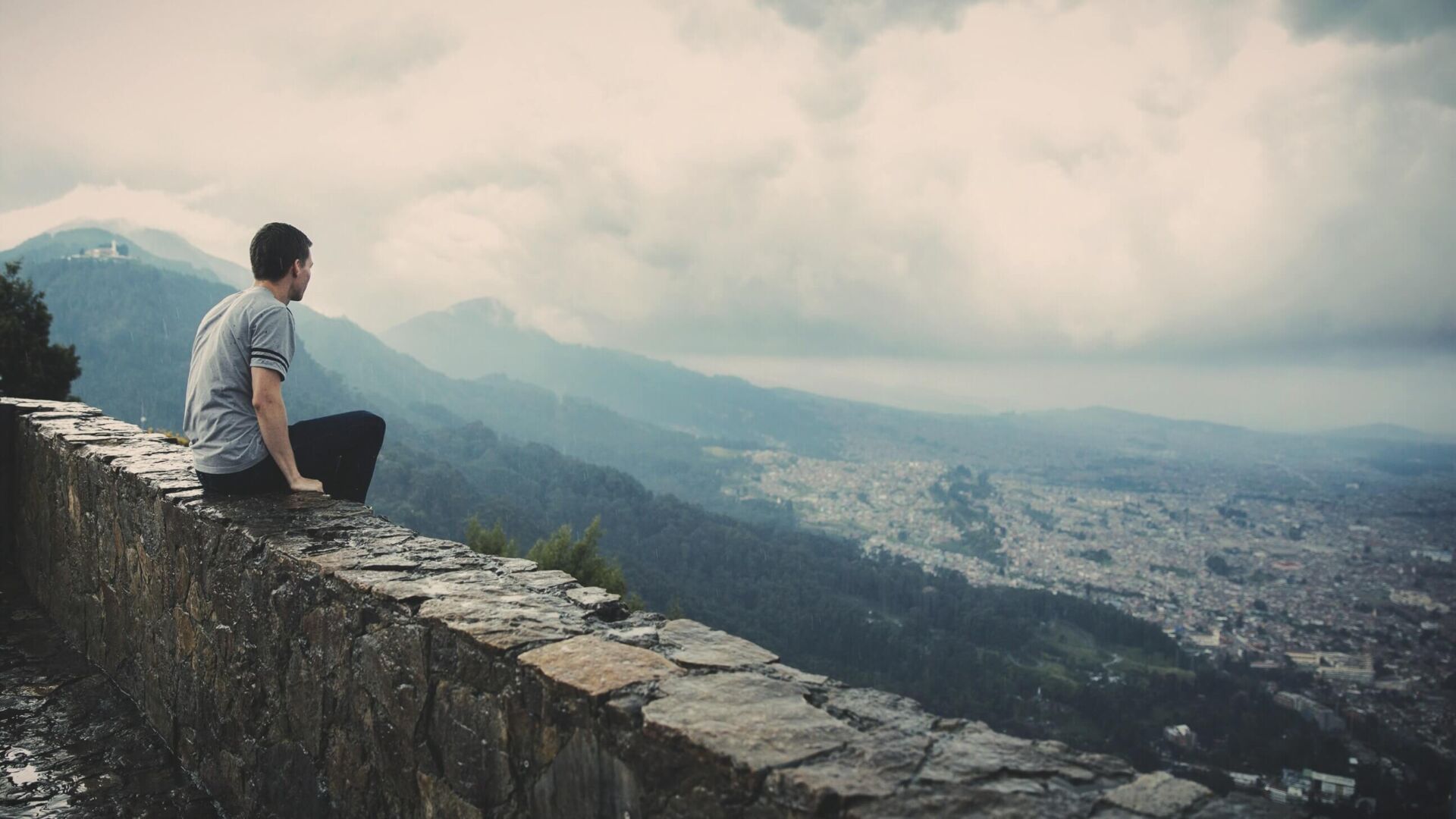 man sitting on wall looking over city