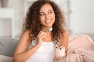 Young woman eating tasty yogurt at home